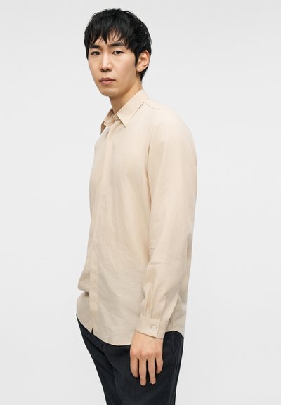 Μπεζ πουκάμισο με μακριά μανίκια και γιακά, μανσέτες με κουμπιά, λείο ύφασμα και άνετη εφαρμογή, συνδυασμένο με σκούρο παντελόνι με ρίγες.