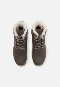 Brown leather boots with a fluffy white lining and patterned laces. Features gold eyelets and a rubber sole for traction.