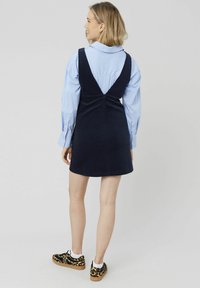 Robe salopette en velours côtelé bleu marine avec un dos en V, associée à une chemise rayée bleu clair et des baskets à imprimé léopard noir et brun.