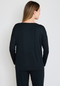 Zwarte langemouwen shirt met een losse pasvorm, brede halslijn en zachte stof. Heeft verlaagde schouders en een licht gebogen zoom aan de achterkant.