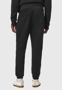 Pantalones deportivos negros de algodón, con dos bolsillos traseros, puños elásticos y un corte relajado. Llevados con zapatillas blancas y beige.