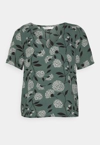 Grön blommig blus med korta ärmar, V-ringning, svarta och vita blommönster samt bladdetaljer på en strukturerad tyg.