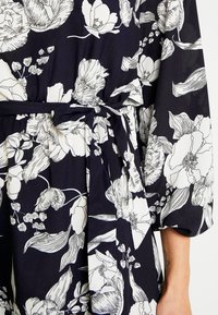 Navy fabric featuring large, white floral patterns with detailed outlines. Includes a fabric belt for cinching at the waist.