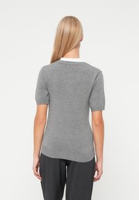 Siv svetrov s kratkimi rokavi in okroglo ovratnikom ter rebrastim robom. Mehka tekstura, prilegajoča oblika in diskretni pleten vzorec. Bele notranje ovratnik je viden.