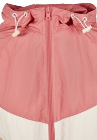 Lekki, różowy wiatrówka z zamkiem błyskawicznym, regulowanym kapturem ze sznurkiem i kontrastującą białą dolną częścią. Gładka, teksturowana tkanina.