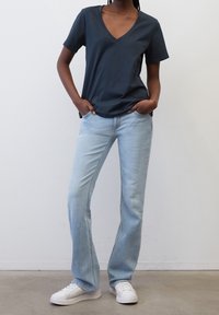 Marineblå v-hals t-shirt parret med lyseblå lige ben jeans og hvide sneakers. Stof ser glat ud; jeans har subtile lysninger.