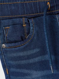 Denima hosen ar elastīgu jostasvietu, auklu, priekšējo kabatu, tumši zilu krāsu un kontrastējošu oranžu adījumu detaļu.