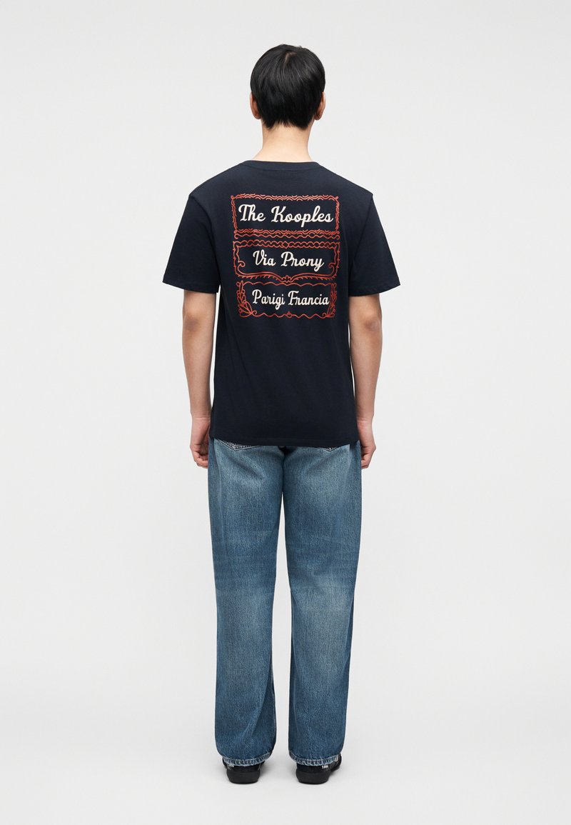 Black cotton t-shirt with red embroidered text on the back: "The Kooples," "Via Prony," and "Parigi Francia." Casual design with short sleeves.