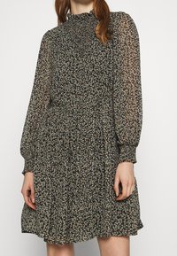 Robes noires à motifs floraux avec de longues manches transparentes, un col smocké et une jupe évasée. Présente de petits motifs floraux colorés sur l'ensemble.