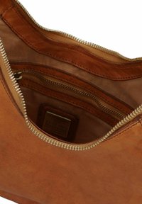 Interno di una borsa in pelle tan con una zip dorata, foderatura in tessuto, molteplici scomparti per l'organizzazione e un'etichetta del marchio visibile.