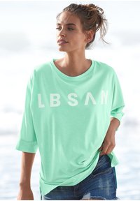 Mint green, oversized t-shirt made from soft fabric, featuring bold white lettering "LBSAN." Rolled sleeves and relaxed fit.