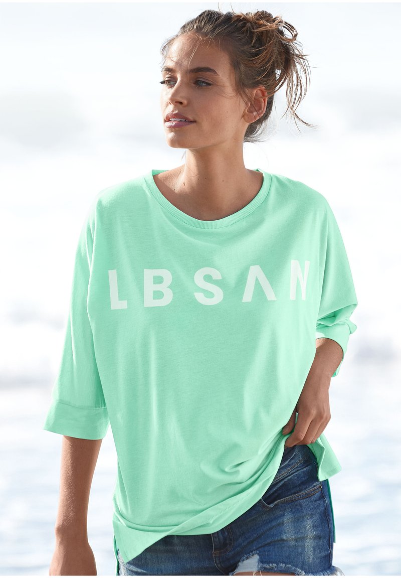 Mint green, oversized t-shirt made from soft fabric, featuring bold white lettering "LBSAN." Rolled sleeves and relaxed fit.