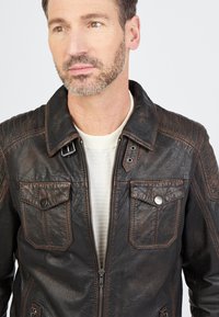 Braune Lederjacke mit Reißverschluss, zwei Brusttaschen und gestickten Details. Verfügt über einen klassischen Kragen und eine strukturierte Oberfläche.