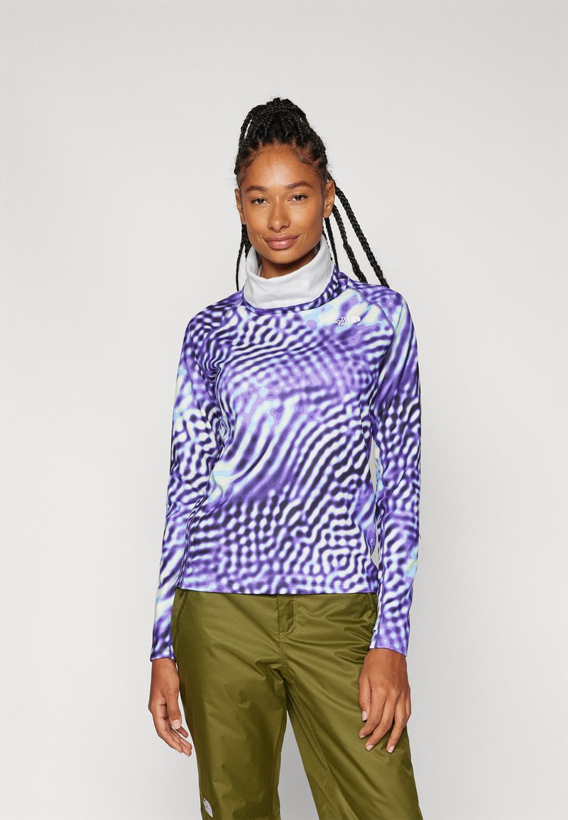 Pikend varrukatega topp, millel on lilla ja must laineline muster. Materjal näeb välja sile ning kaelus on kõrge. Sobitatud roheliste pükstega.