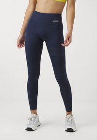 Marina leggings tillverkade av stretchigt tyg med hög midja. Har mesh-liknande ränder på sidorna och kombineras med grå träningsskor.