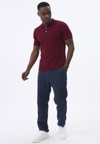 Bordeaux polo shirt med korte ærmer og krave, parret med marineblå bukser og hvide sneakers. Glat stof med subtil logo-detalje.