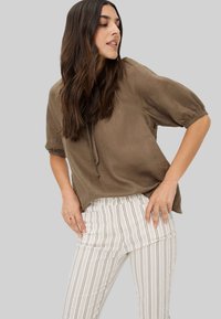 Bruine, korte mouw top met een trekkoorddetail, gecombineerd met gestreepte, aansluitende broek in witte, beige en zachte bruine tinten.