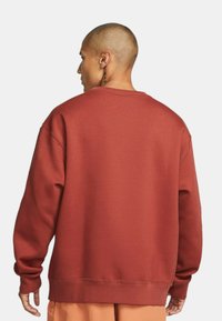 Czerwona bluza z okrągłym dekoltem, z długimi rękawami i ściągaczami. Miękka, teksturowana tkanina. Posiada luźny krój oraz płaskie szwy wzdłuż krawędzi.