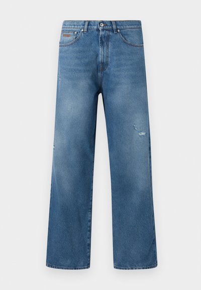 Jean en denim bleu avec une coupe droite, légère usure sur la cuisse droite, style cinq poches, et taille avec fermeture à boutons.