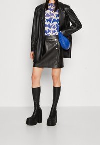 Mustat keinonahkaiset bleiseri, kuviollinen sininen paita, mustat nahkakehykset, sininen käsilaukku ja polveen yltävät mustat platform-nilkkurit.