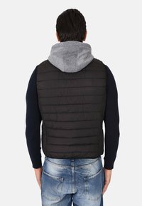 Gilet trapuntato nero con cappuccio grigio, caratterizzato da un design minimalista, abbinato a jeans blu sbiaditi, con tasche posteriori visibili e maniche a costine.