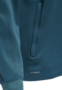 Manica e lato giacca in tessuto blu con tasca verticale e scritta "BEECOOL" vicino all'orlo su materiale dalla texture liscia.