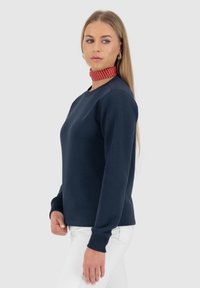 Navyblauwe sweatshirt met lange mouwen en een ronde hals, voorzien van geribbelde manchetten. Gecombineerd met een rode stippen choker.