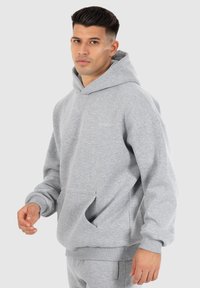 Histoire grise avec une poche kangourou, des poignets côtelés et une coupe décontractée. Tissu doux et design minimal. Pas de logos ou de motifs visibles.