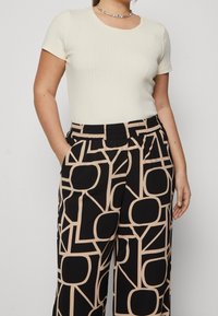 Top corto de manga corta de canalé crema combinado con pantalones negros que presentan un patrón geométrico beige, mostrando un ajuste relajado y una cinturilla elástica.