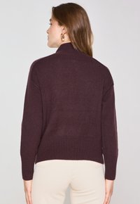 Pull en maille bordeaux avec un col montant, des poignets et un ourlet côtelés, et une coupe décontractée. Présente une texture douce et un design à épaule tombante.