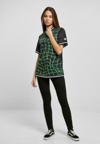 Sort kortærmet skjorte med et grønt rutenetmønster, udstyret med en knaplukning og hvid kant. Parret med sorte leggings og sorte sneakers.