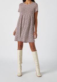 Robe à manches courtes imprimée de fleurs en bourgogne avec une taille froncée. Associée à des bottes blanches à talons hauts et lisses, au design ajusté.