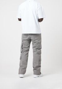 Pantalon cargo gris avec plusieurs poches, porté avec un t-shirt blanc à manches courtes. Le matériau semble être du coton, avec une coupe décontractée et une coupe droite.