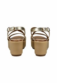 Zlaté metalické sandály na tenkých páscích s masivním béžovým blokovým podpatkem a hladkým hnědým stélkou; nastavitelné sponové zapínání na pásku kolem kotníku pro lepší přizpůsobení.