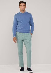 Lichtblauwe trui van breiwerk, gedragen over een wit-blauw gestreepte blouse. Lichtgroene broek en donkere sneakers maken de outfit compleet.