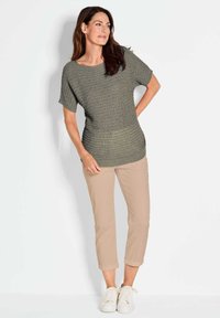 Olijfgroene gebreide top met korte mouwen, gecombineerd met lichtbeige cropped pants en witte sneakers, weergegeven tegen een effen achtergrond.
