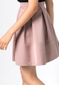 Dammrosa knälång kjol gjord av slät tyg, med en figursydd midja och plisserad design för en utsvängd siluett.