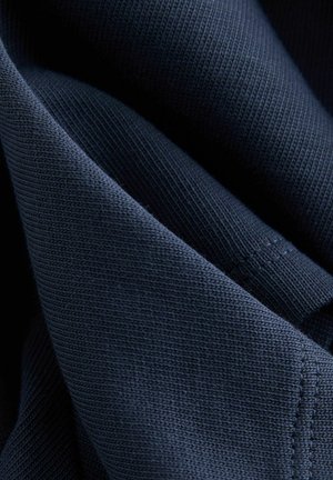 Marineblåt bomuldsstof med en glat tekstur, der har et tæt vævet mønster og synlige sømme langs kanterne.