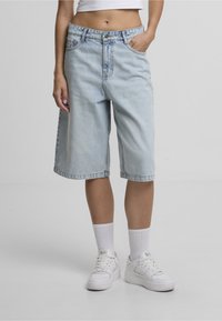 Lyseblå denimshorts med løs pasform, knælængde, med fem lommer, bæltestropper og knaplukning foran. Bruges med hvide sneakers.