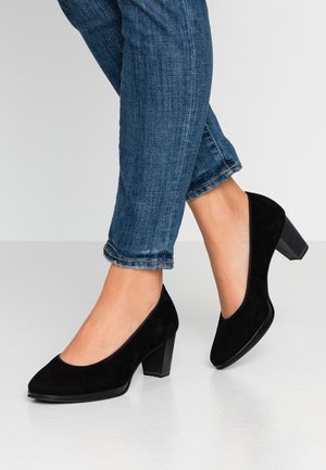 Sorte flade højhælede pumps i ruskind med rund tå og en struktureret blokk hæl, båret med opkrøllede blå denim jeans.