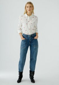White button-up shirt with red lips pattern, paired with high-waisted blue denim jeans featuring large front pockets and black ankle boots.