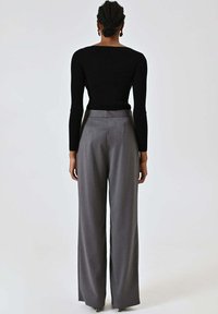 Top nero a maniche lunghe a coste abbinato a pantaloni grigi a vita alta e gamba larga. Tessuto liscio con finitura pulita e design minimalista.