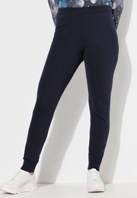 Granatowe spodnie dresowe wykonane z miękkiej mieszanki bawełny, charakteryzujące się dopasowanym krojem, elastycznym pasem i ściągaczami na końcach nogawek, zestawione z białymi sneakersami.