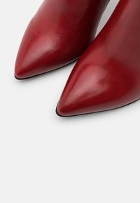 Tacchi a spillo rossi in pelle, con punta affusolata, texture liscia e finitura lucida. Nessun hardware o motivo visibile, con un design elegante e minimal.