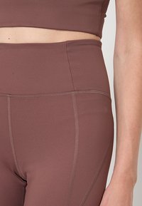 Barna aktív viselet készlet, amely egy rövidített felsőből és magas derekú leggingsből áll. Simaság, nyújtható anyag finom varrási részletekkel.