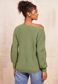 Grüner Strickpullover mit lockerer Passform, weitem Ausschnitt und Ballonärmeln. Verfügt über eine gerippte Textur und ein weiches Finish. Kombiniert mit blauen Jeans.