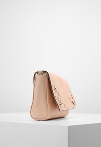 Borsa a tracolla in pelle beige con patta, caratterizzata da motivi floreali tagliati al laser, bordi arrotondati e una superficie liscia.