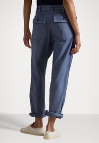 Pantalons bleu clair avec des poignets roulés, deux poches arrières avec fermetures à bouton, et une coupe décontractée en tissu en coton texturé.