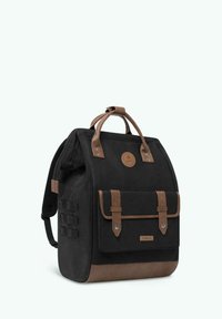 Zaino in tela nera con accenti in pelle marrone, maniglia superiore, tasca frontale con linguetta e spallacci regolabili. Presenta una placca con il logo.