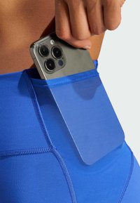 Modré športové legíny s bezpečným sieťovaným vreckom na smartfón. Materiál je hladký a má zosilnené švy pozdĺž stehov.